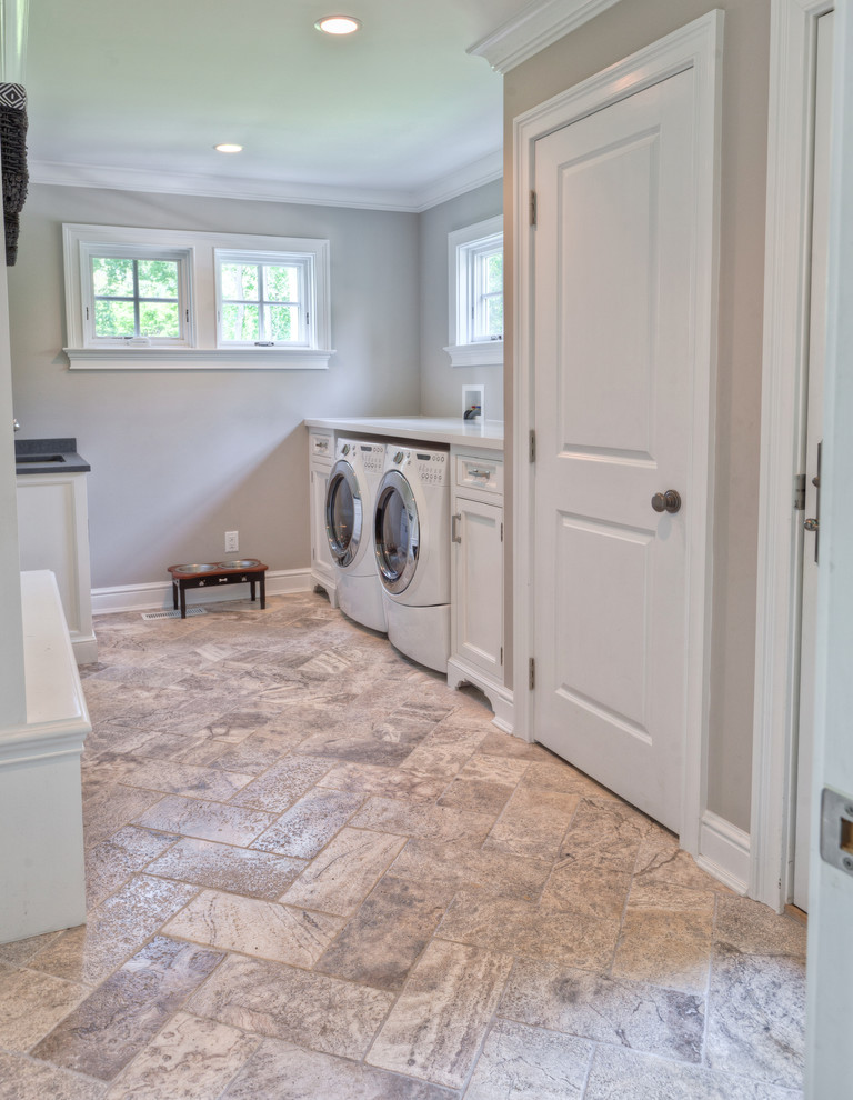Photo of a large traditional galley utility room in New York with an undermount sink, recessed-panel cabinets, white cabinets, solid surface benchtops, beige walls, travertine floors, a side-by-side washer and dryer, beige floor and white benchtop.
