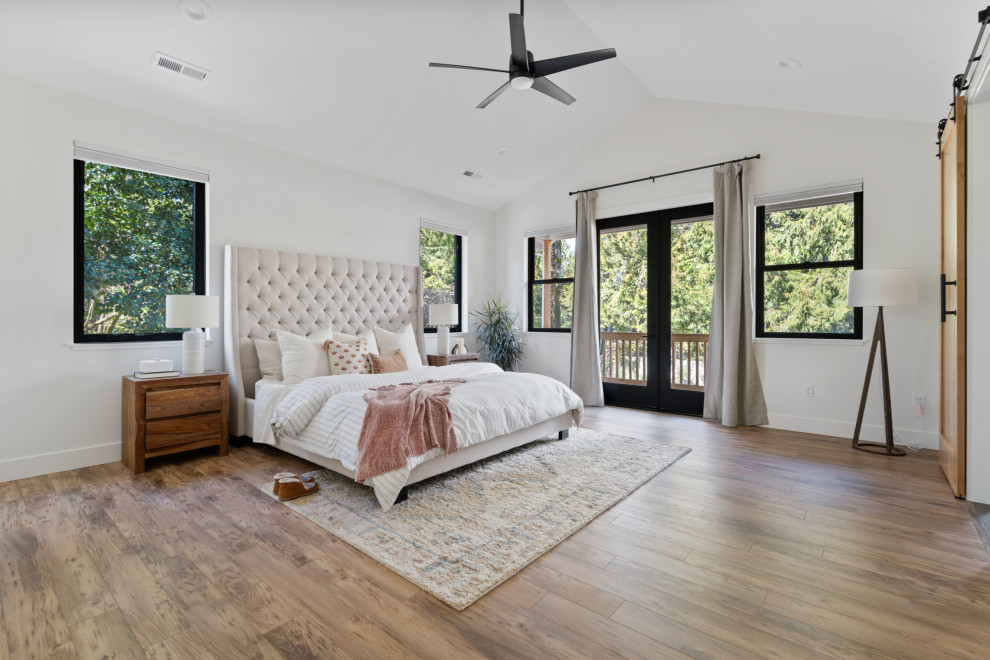 На фото: хозяйская спальня среднего размера в стиле кантри с белыми стенами, полом из ламината, коричневым полом и деревянными стенами
