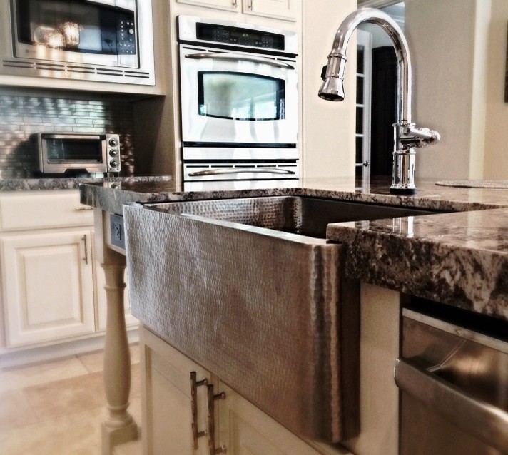 Inspiration for a mid-sized transitional l-shaped travertine floor eat-in kitchen remodel in Houston with a farmhouse sink, raised-panel cabinets, white cabinets, granite countertops, metallic backsplash, metal backsplash, stainless steel appliances and an island