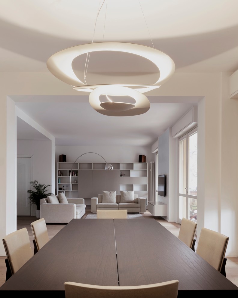 This is an example of a modern open plan dining in Milan with white walls and light hardwood floors.