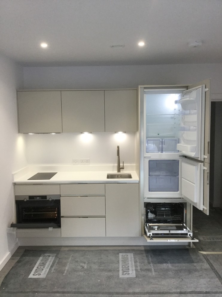 Photo of a small modern galley open plan kitchen in Hampshire with a drop-in sink, flat-panel cabinets, grey cabinets, quartzite benchtops, multi-coloured splashback, glass sheet splashback, stainless steel appliances, laminate floors, no island, grey floor and white benchtop.