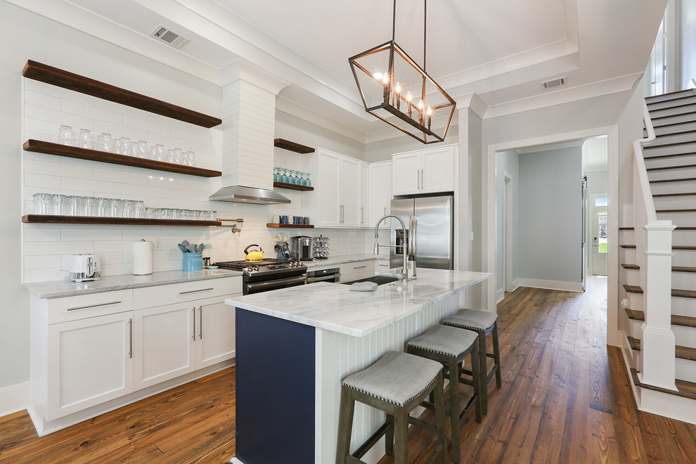 Design ideas for a transitional u-shaped kitchen in New Orleans with shaker cabinets, white cabinets, white splashback, subway tile splashback, stainless steel appliances, medium hardwood floors, with island and brown floor.