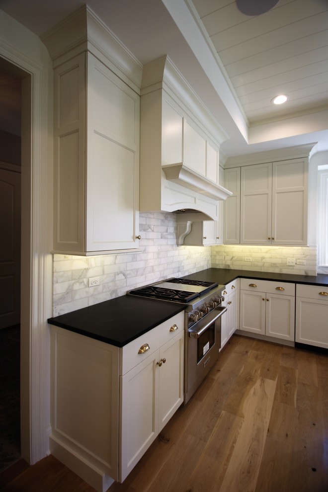 This is an example of a large arts and crafts open plan kitchen in Chicago with an undermount sink, recessed-panel cabinets, white cabinets, stainless steel appliances, medium hardwood floors, brown floor, solid surface benchtops, grey splashback, marble splashback and black benchtop.