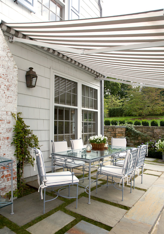 Inspiration for a mid-sized traditional side yard patio in New York with natural stone pavers and an awning.