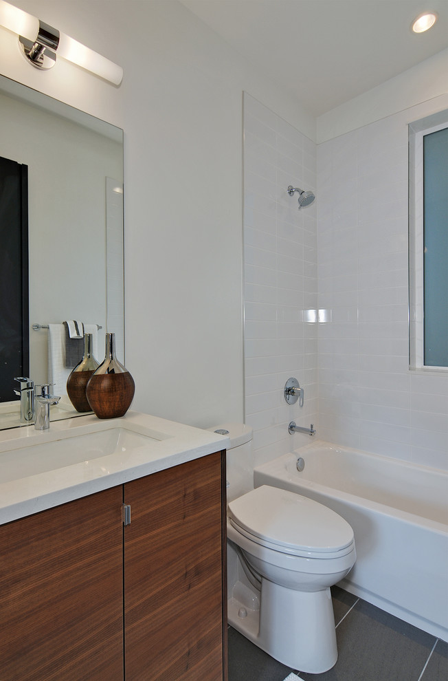 This is an example of a mid-sized midcentury bathroom in Seattle with flat-panel cabinets, medium wood cabinets, an alcove tub, a shower/bathtub combo, a one-piece toilet, white tile, ceramic tile, white walls, ceramic floors, an undermount sink, engineered quartz benchtops, grey floor, a shower curtain and white benchtops.