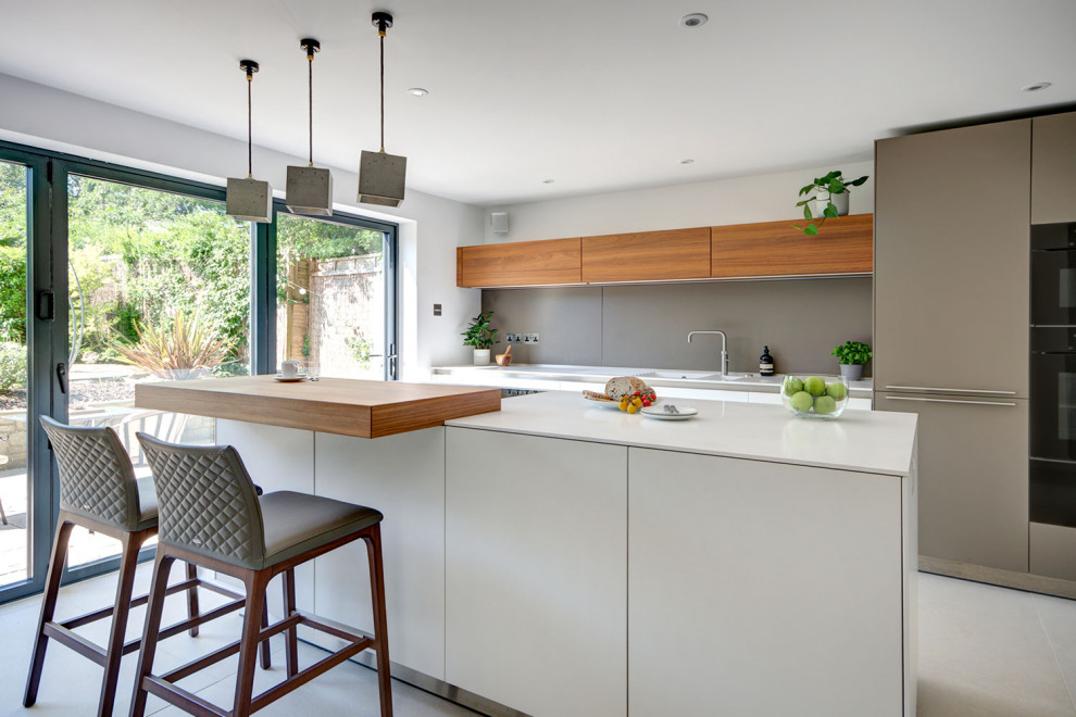 Inspiration for a medium sized contemporary single-wall kitchen/diner in Wiltshire with an integrated sink, flat-panel cabinets, white cabinets, composite countertops, grey splashback, black appliances, porcelain flooring, an island and white worktops.