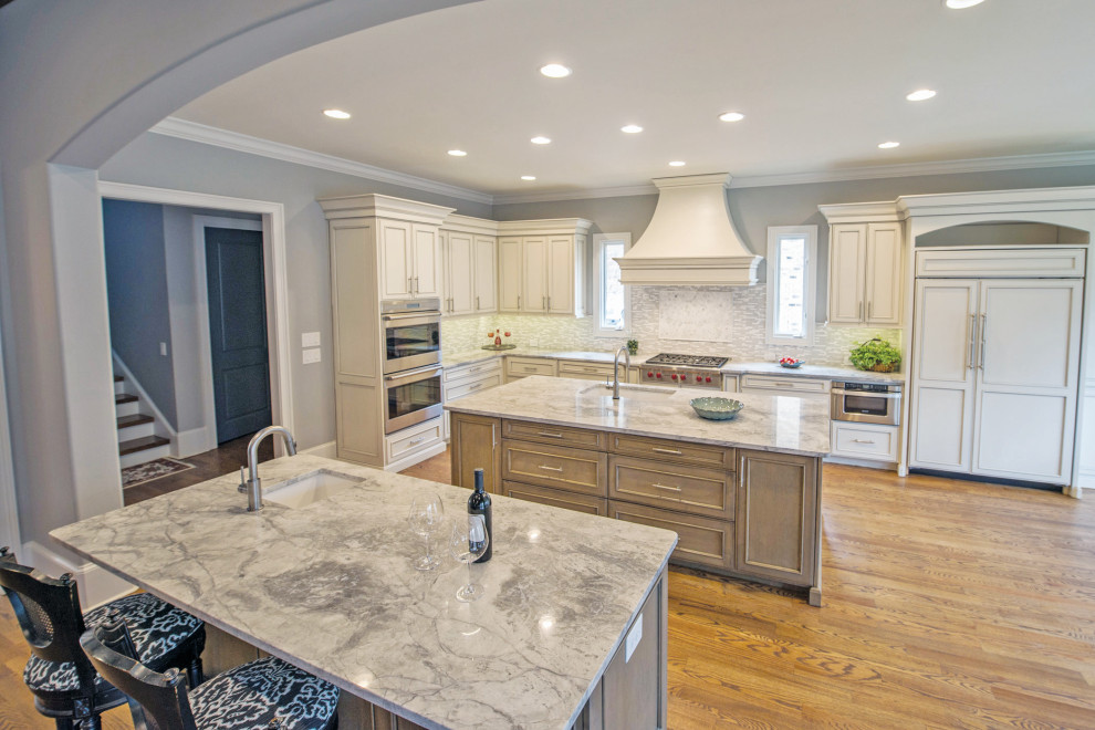 Example of a large transitional l-shaped medium tone wood floor and brown floor eat-in kitchen design with an undermount sink, gray backsplash, stainless steel appliances, two islands, beige cabinets, marble countertops and glass tile backsplash