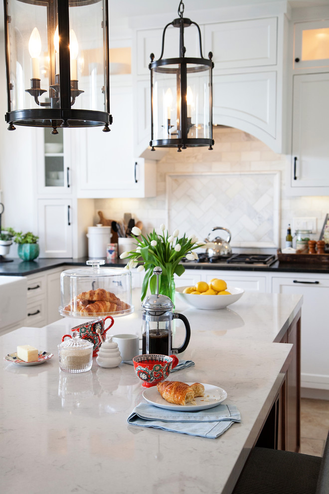 Inspiration for a mid-sized transitional u-shaped kitchen in San Diego with a farmhouse sink, recessed-panel cabinets, white cabinets, soapstone benchtops, white splashback, stone tile splashback, stainless steel appliances, travertine floors and with island.