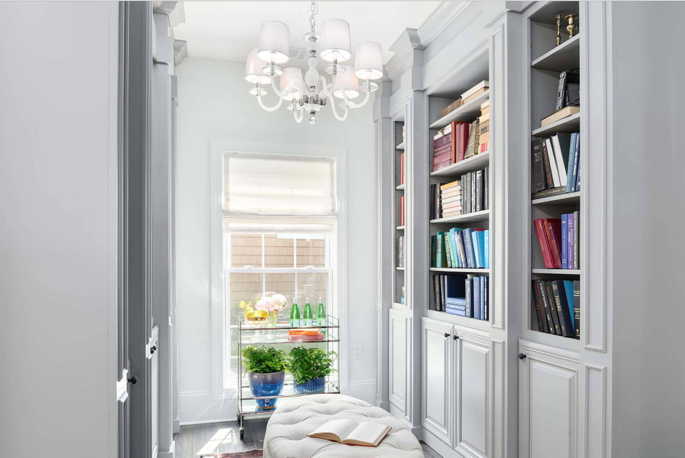 Photo of a mid-sized transitional home office in DC Metro with a library, white walls, medium hardwood floors, no fireplace, grey floor and a freestanding desk.