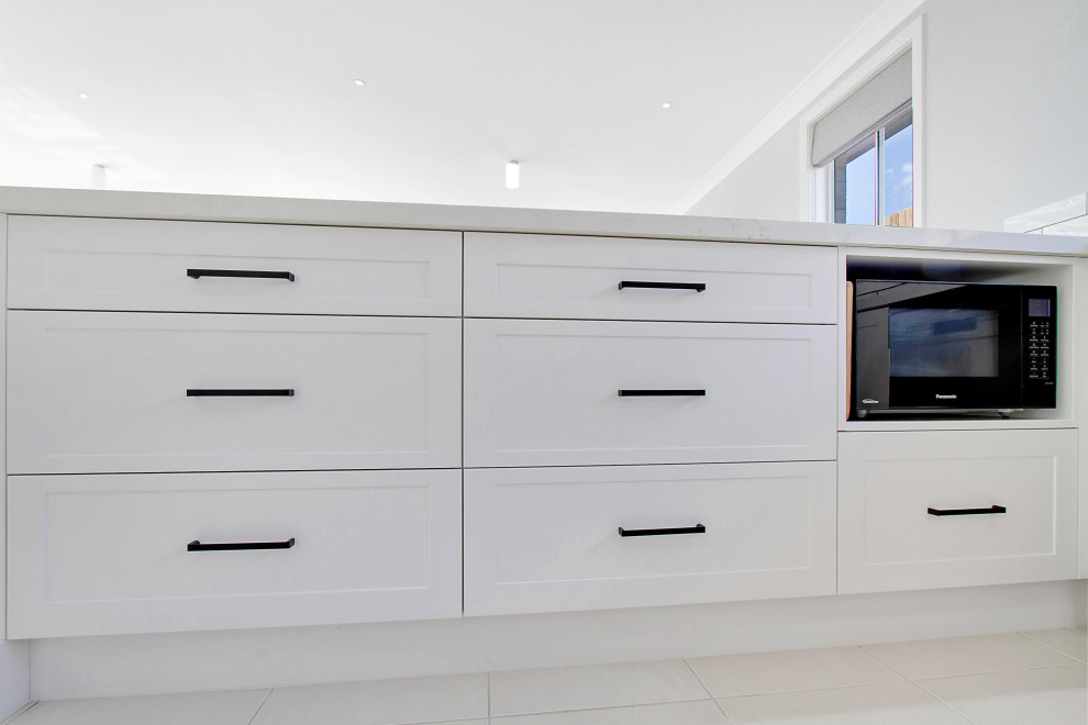 Photo of a mid-sized contemporary u-shaped kitchen pantry in Sydney with a double-bowl sink, shaker cabinets, white cabinets, quartz benchtops, white splashback, subway tile splashback, black appliances, a peninsula, white floor and white benchtop.