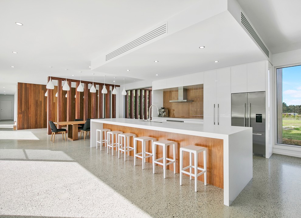 This is an example of an expansive contemporary galley kitchen in Geelong with an undermount sink, flat-panel cabinets, white cabinets, quartz benchtops, timber splashback, stainless steel appliances, concrete floors and with island.