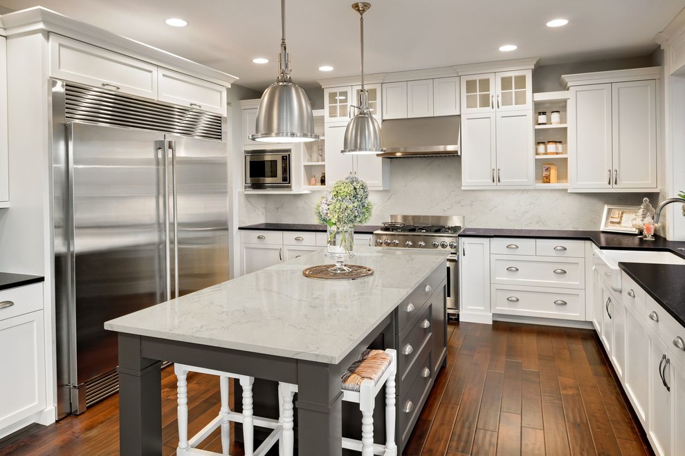 Kitchen - transitional l-shaped medium tone wood floor kitchen idea in Toronto with quartz countertops, a farmhouse sink, shaker cabinets, white cabinets, white backsplash, stone slab backsplash, stainless steel appliances and an island