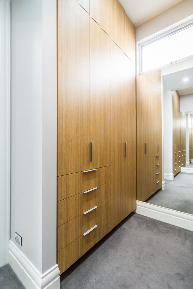 Photo of a mid-sized modern gender-neutral built-in wardrobe in Melbourne with flat-panel cabinets, medium wood cabinets, carpet and grey floor.