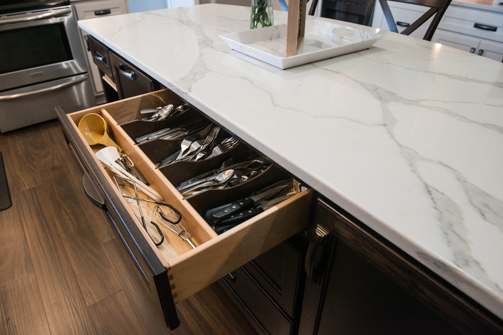 Large transitional u-shaped laminate floor and brown floor eat-in kitchen photo with a double-bowl sink, shaker cabinets, white cabinets, quartz countertops, gray backsplash, subway tile backsplash, stainless steel appliances, an island and white countertops