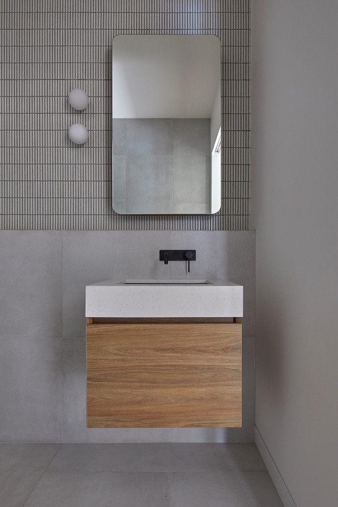 This is an example of a small modern cloakroom in Melbourne with light wood cabinets, a wall mounted toilet, grey tiles, mosaic tiles, grey walls, a submerged sink, engineered stone worktops, grey floors, grey worktops and a floating vanity unit.