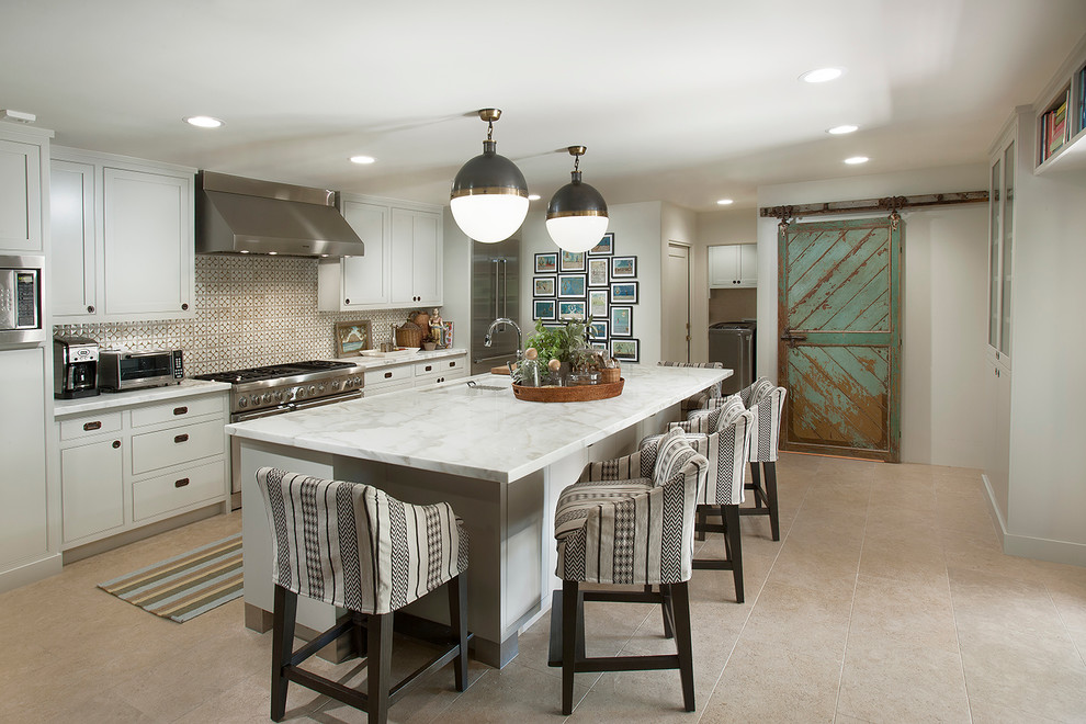 Photo of a mid-sized country galley kitchen in Phoenix with an undermount sink, flat-panel cabinets, white cabinets, marble benchtops, white splashback, stainless steel appliances, travertine floors and with island.