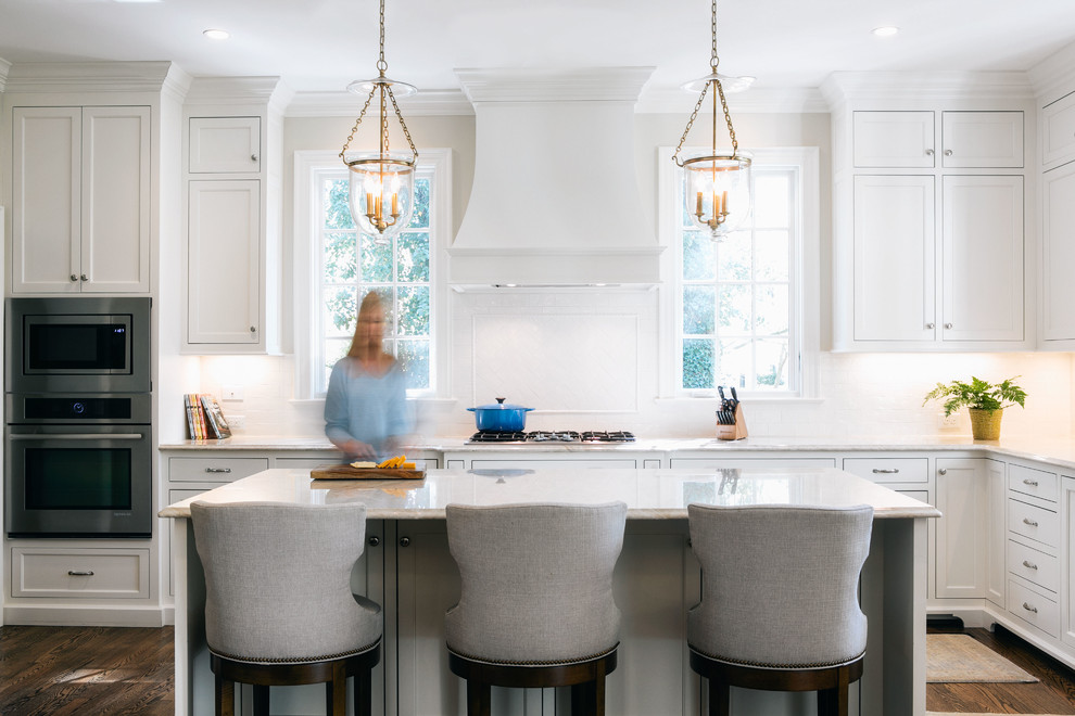Photo of a traditional l-shaped kitchen in Raleigh with shaker cabinets, white cabinets, white splashback, stainless steel appliances, dark hardwood floors and with island.