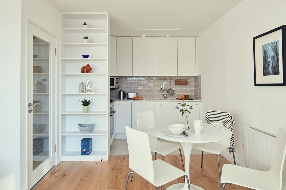 This is an example of a small contemporary l-shaped open plan kitchen in Dublin with an undermount sink, flat-panel cabinets, white cabinets, quartz benchtops, grey splashback, subway tile splashback, ceramic floors, no island and stainless steel appliances.