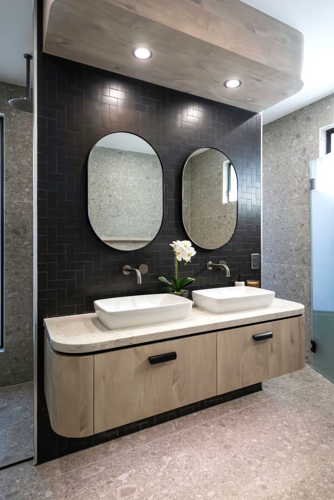 Photo of a contemporary bathroom in Sydney with flat-panel cabinets, light wood cabinets, black tile, a vessel sink, grey floor, white benchtops, a double vanity and a floating vanity.