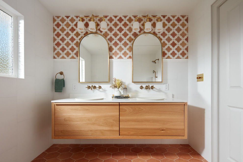 Photo of a mediterranean bathroom in San Francisco with flat-panel cabinets, medium wood cabinets, white tiles, orange walls, terracotta flooring, a built-in sink, orange floors, white worktops, double sinks and a floating vanity unit.