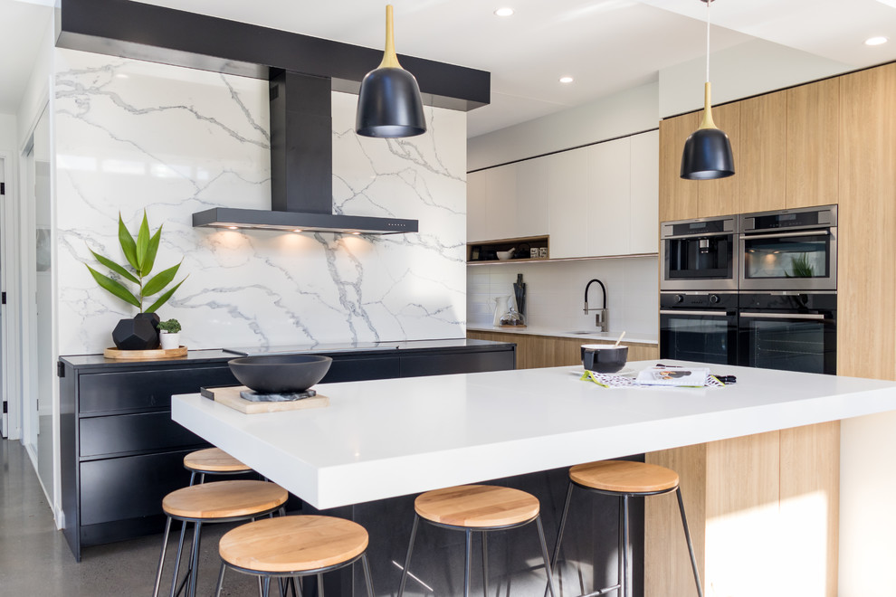 This is an example of a contemporary l-shaped open plan kitchen in Sunshine Coast with flat-panel cabinets, light wood cabinets, white splashback, stainless steel appliances, with island, grey floor, an undermount sink, quartz benchtops and concrete floors.