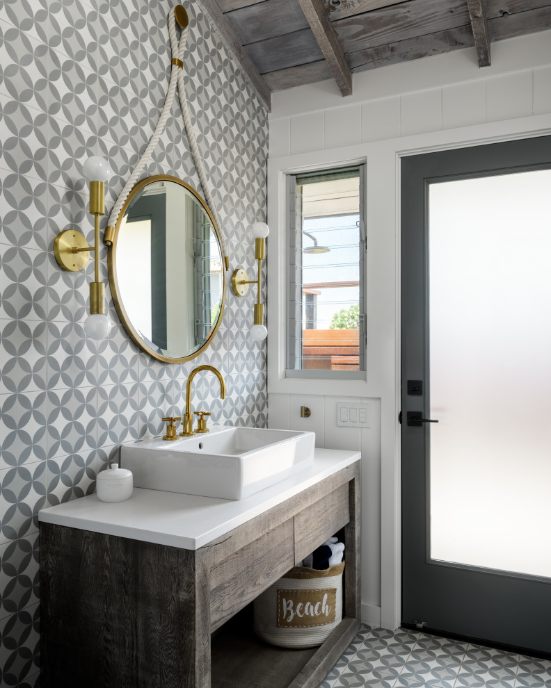 Mid-sized beach style powder room in Hawaii with flat-panel cabinets, distressed cabinets, a one-piece toilet, gray tile, cement tile, white walls, cement tiles, a pedestal sink, engineered quartz benchtops, grey floor, white benchtops, a freestanding vanity, exposed beam and panelled walls.