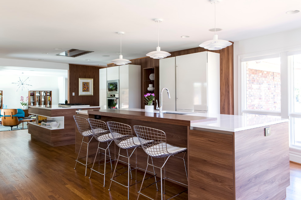 Design ideas for a mid-sized contemporary galley open plan kitchen in Charlotte with flat-panel cabinets, white cabinets, stainless steel appliances, medium hardwood floors and multiple islands.