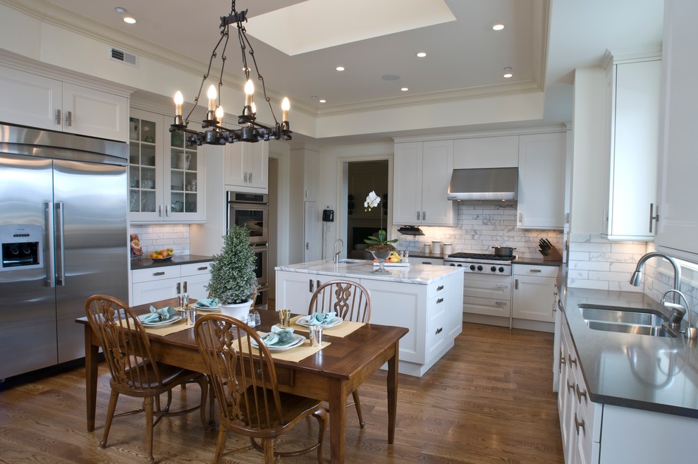 Example of a large transitional u-shaped medium tone wood floor eat-in kitchen design with an undermount sink, recessed-panel cabinets, white cabinets, marble countertops, white backsplash, stone tile backsplash, stainless steel appliances and an island