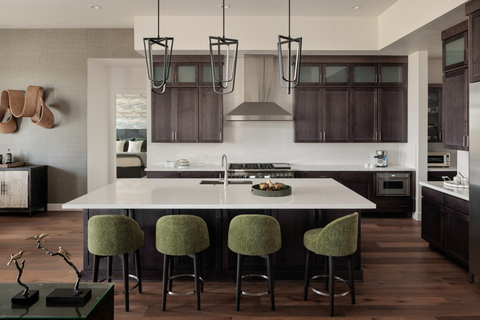 Eat-in kitchen - mid-sized transitional l-shaped medium tone wood floor and brown floor eat-in kitchen idea with an undermount sink, shaker cabinets, brown cabinets, quartzite countertops, white backsplash, mosaic tile backsplash, stainless steel appliances, an island and white countertops