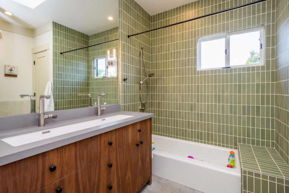 Inspiration for a kids bathroom in San Francisco with flat-panel cabinets, medium wood cabinets, an alcove tub, a shower/bathtub combo, green tile, white walls, a trough sink, grey benchtops, a double vanity and a built-in vanity.