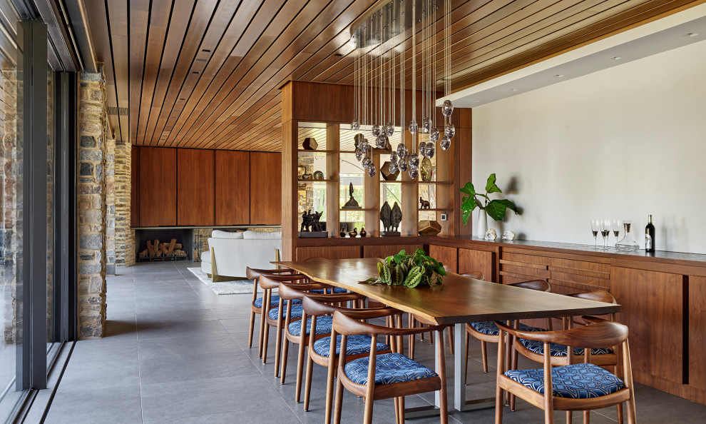 Immagine di una sala da pranzo moderna con pavimento in gres porcellanato, cornice del camino in pietra, pavimento grigio e soffitto in legno
