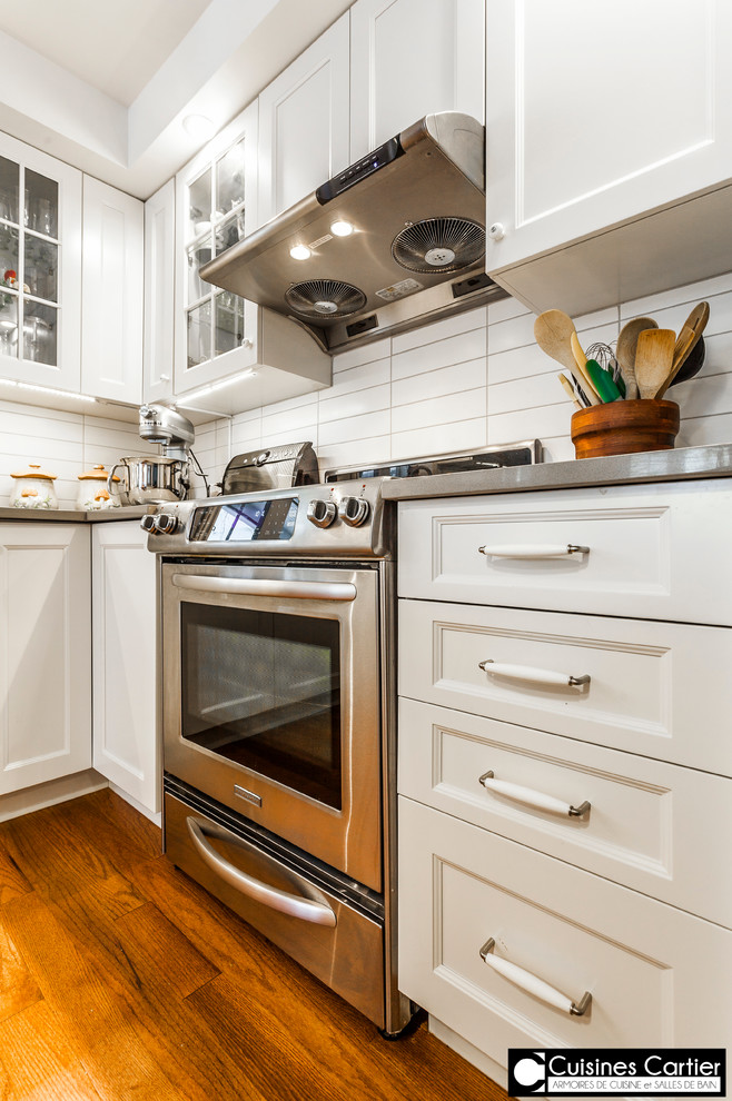 Eat-in kitchen - large transitional medium tone wood floor eat-in kitchen idea in Montreal with a double-bowl sink, shaker cabinets, white cabinets, quartzite countertops, white backsplash, ceramic backsplash, stainless steel appliances and an island