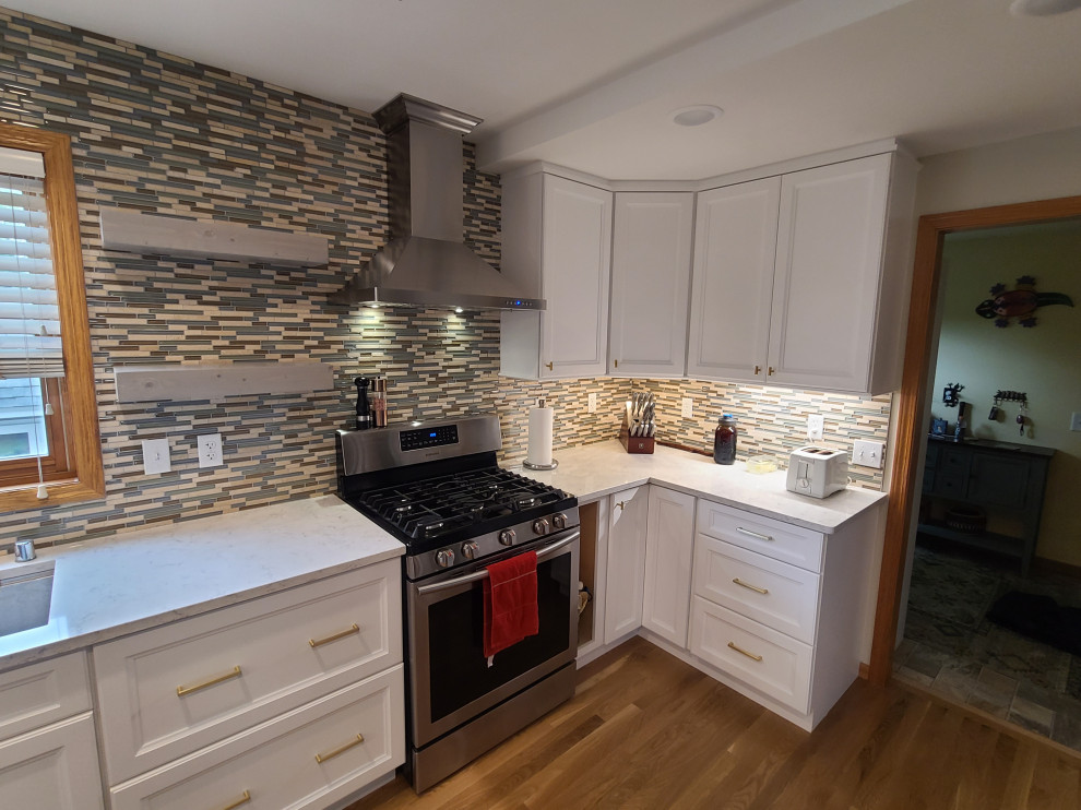 Cette photo montre une cuisine américaine chic en L de taille moyenne avec un placard à porte shaker, des portes de placard blanches et un plan de travail en quartz modifié.