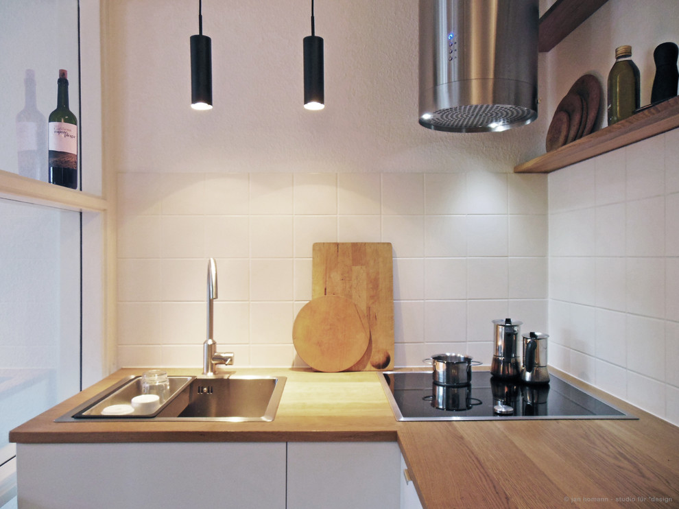 Kleine, Geschlossene Moderne Küche ohne Insel in U-Form mit Einbauwaschbecken, flächenbündigen Schrankfronten, weißen Schränken, Arbeitsplatte aus Holz, Küchenrückwand in Weiß, Rückwand aus Keramikfliesen, Küchengeräten aus Edelstahl und Keramikboden in Hamburg