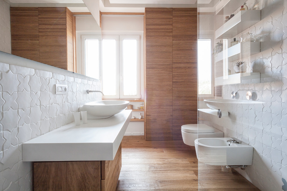 This is an example of a mid-sized modern bathroom in Other with flat-panel cabinets, light wood cabinets, a wall-mount toilet, white tile, ceramic tile, white walls, light hardwood floors and a vessel sink.