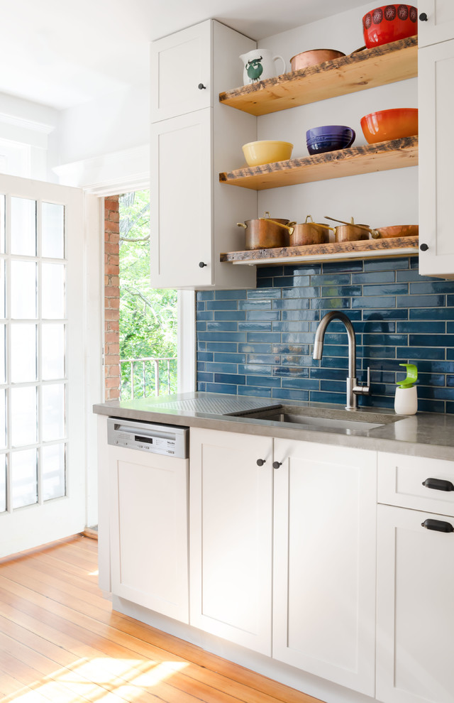 Photo of a mid-sized eclectic u-shaped separate kitchen in Boston with an undermount sink, recessed-panel cabinets, white cabinets, concrete benchtops, blue splashback, subway tile splashback, white appliances, light hardwood floors, no island and brown floor.
