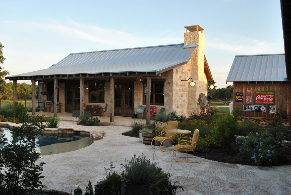 Design ideas for a mid-sized country backyard custom-shaped pool in Austin with a pool house and natural stone pavers.