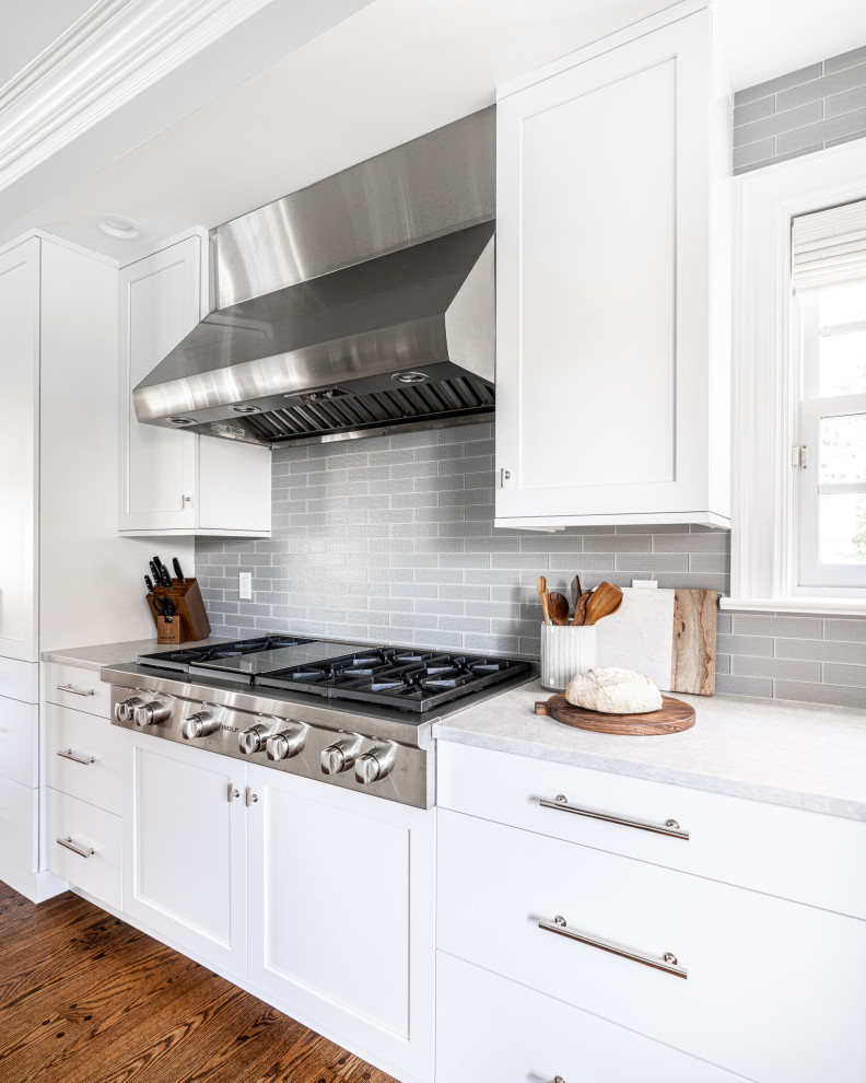 Idéer för att renovera ett stort vintage vit vitt kök, med en undermonterad diskho, skåp i shakerstil, vita skåp, bänkskiva i kvarts, grått stänkskydd, stänkskydd i glaskakel, integrerade vitvaror, mörkt trägolv, en köksö och brunt golv