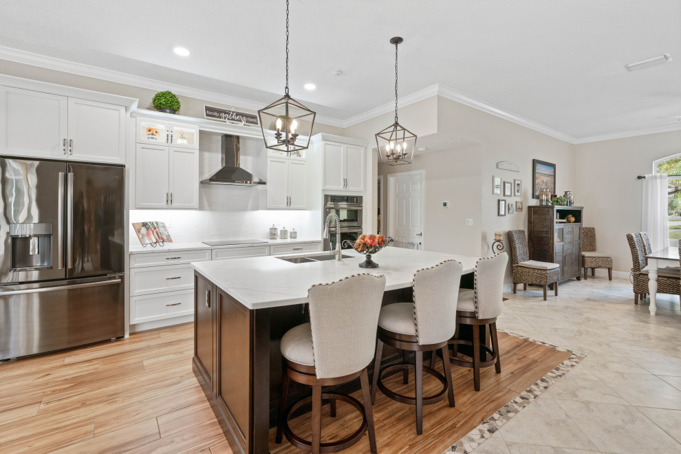 Mid-sized transitional single-wall porcelain tile and multicolored floor eat-in kitchen photo with a double-bowl sink, shaker cabinets, white cabinets, quartz countertops, white backsplash, porcelain backsplash, stainless steel appliances, white countertops and an island