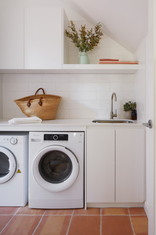 メルボルンにあるお手頃価格の中くらいなモダンスタイルのおしゃれな洗濯室 (ll型、アンダーカウンターシンク、クオーツストーンカウンター、白いキッチンパネル、セラミックタイルのキッチンパネル、テラコッタタイルの床、左右配置の洗濯機・乾燥機、オレンジの床、白いキッチンカウンター) の写真