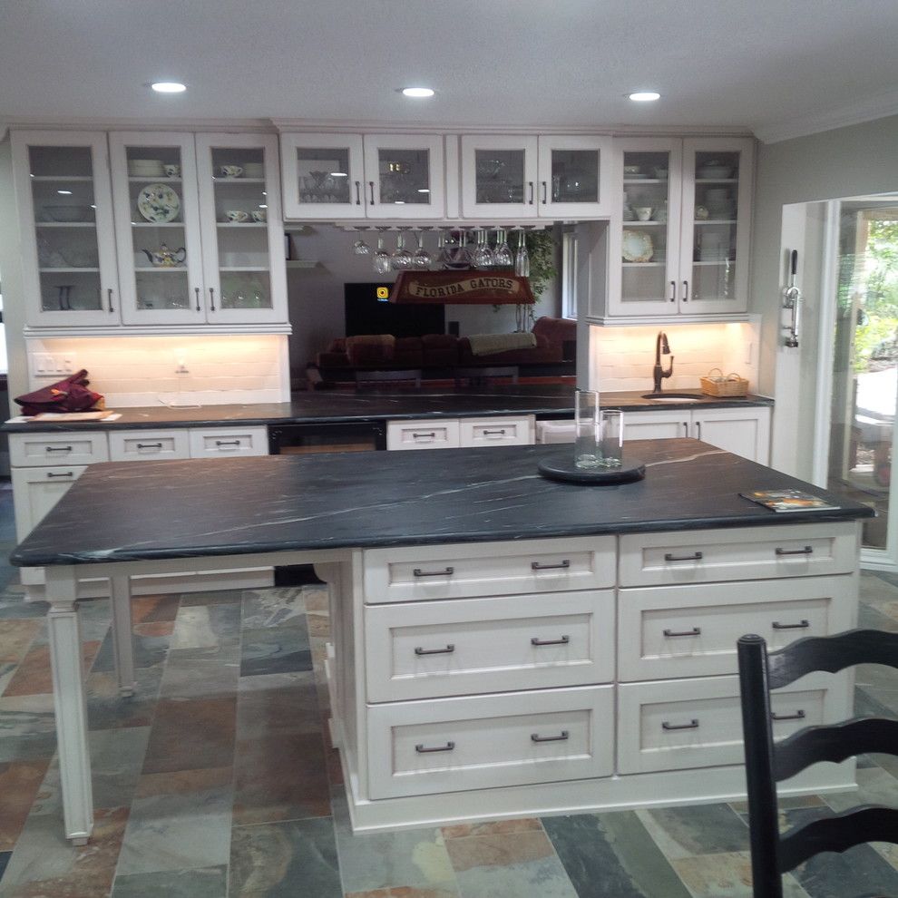 Inspiration for an expansive transitional kitchen in Orlando with a farmhouse sink, recessed-panel cabinets, distressed cabinets, soapstone benchtops, white splashback, subway tile splashback, panelled appliances, slate floors and with island.
