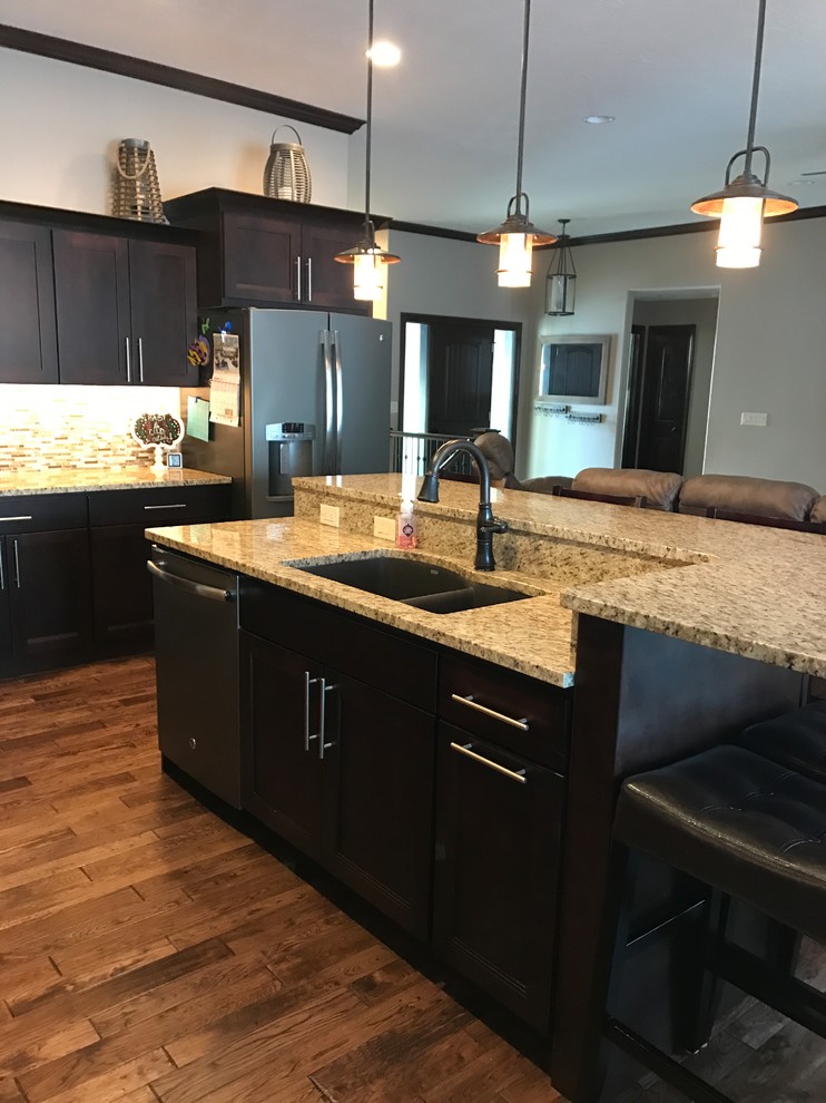 Example of a transitional l-shaped kitchen design with an undermount sink, flat-panel cabinets, dark wood cabinets, granite countertops, multicolored backsplash, ceramic backsplash, stainless steel appliances and an island
