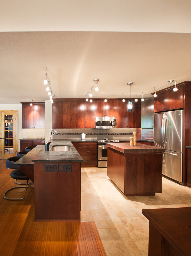 This is an example of a modern u-shaped eat-in kitchen in Minneapolis with an undermount sink, flat-panel cabinets, dark wood cabinets, wood benchtops, beige splashback, stone tile splashback and stainless steel appliances.