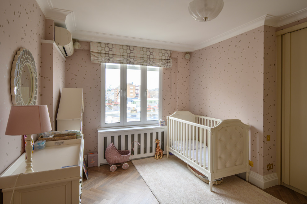 Inspiration for a mid-sized transitional nursery for girls in London with pink walls, medium hardwood floors and brown floor.