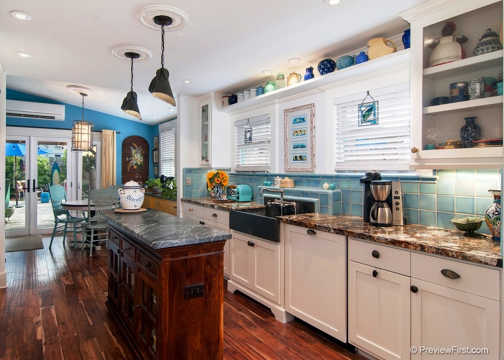 Photo of a small beach style galley open plan kitchen in San Diego with a farmhouse sink, flat-panel cabinets, white cabinets, granite benchtops, multi-coloured splashback, glass tile splashback, coloured appliances, dark hardwood floors, with island and brown floor.