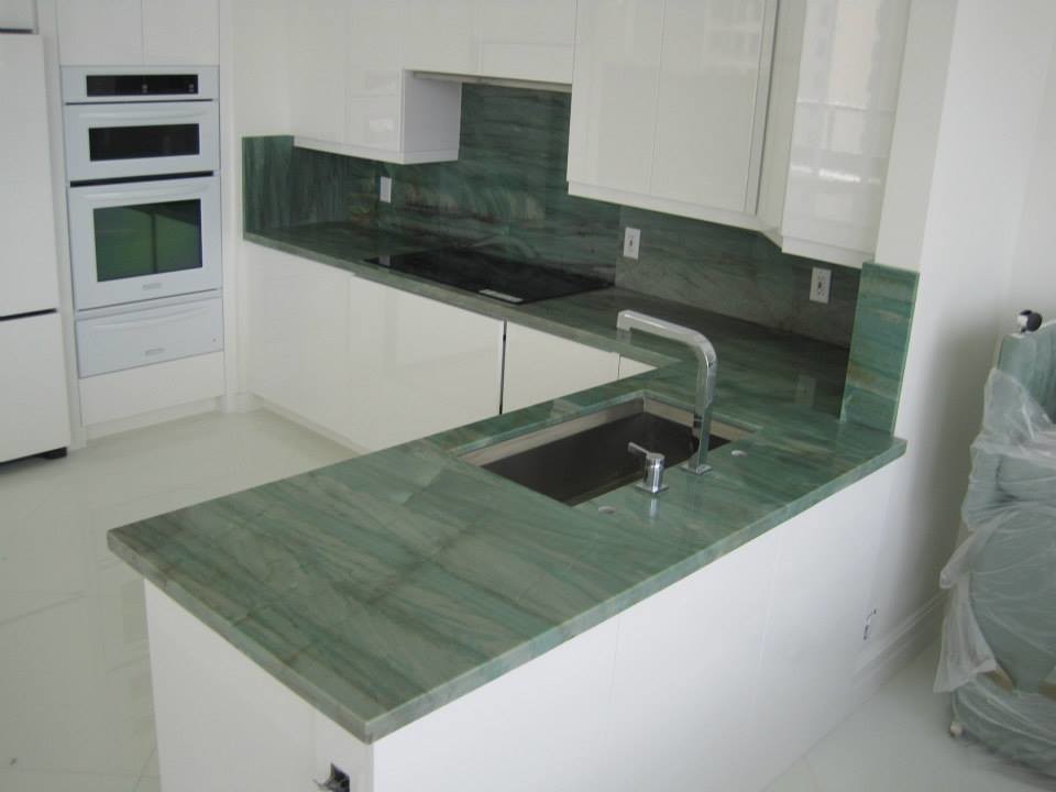 This is an example of a large modern l-shaped separate kitchen in Miami with flat-panel cabinets, medium wood cabinets, granite benchtops, ceramic floors, with island, an undermount sink, green splashback, stone slab splashback, white appliances, white floor and green benchtop.