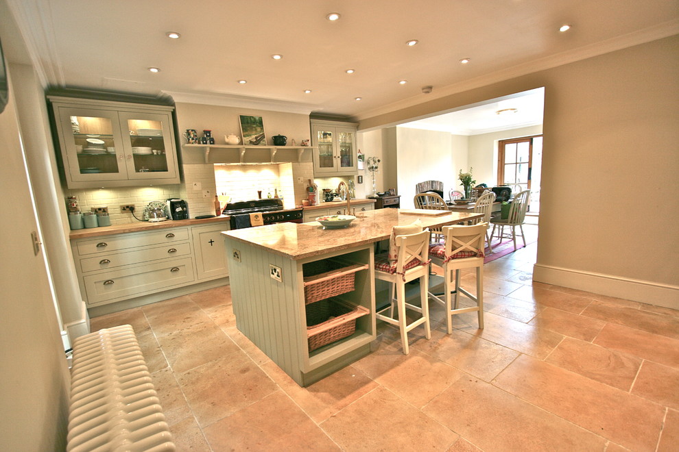 Photo of a large traditional kitchen in London with a farmhouse sink, shaker cabinets, green cabinets, granite benchtops, coloured appliances, travertine floors and with island.