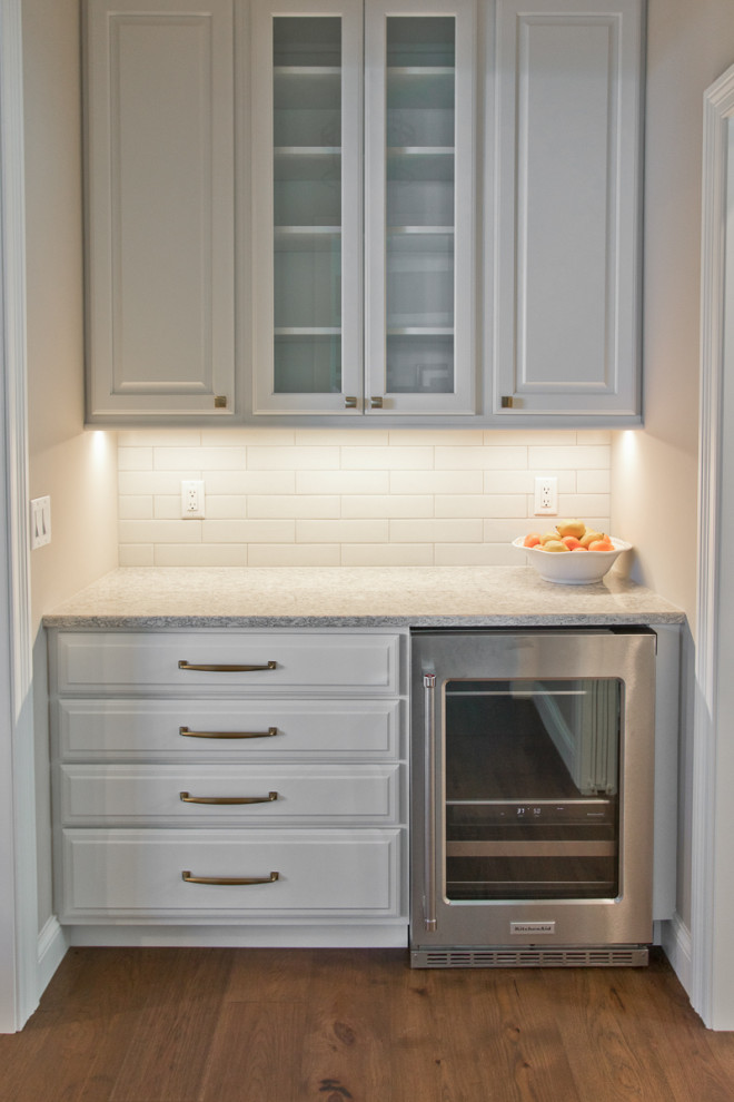 Photo of a transitional kitchen pantry in Other with raised-panel cabinets, white cabinets, quartz benchtops, white splashback, ceramic splashback, stainless steel appliances, medium hardwood floors, brown floor and white benchtop.
