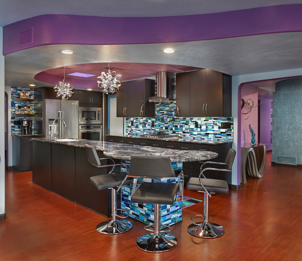 This is an example of a large eclectic l-shaped kitchen in Phoenix with an undermount sink, flat-panel cabinets, granite benchtops, glass tile splashback, stainless steel appliances, medium hardwood floors, with island, brown floor, black cabinets, multi-coloured splashback and grey benchtop.