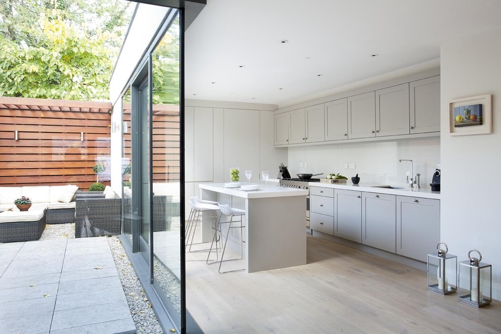 Contemporary l-shaped kitchen in Dublin with an undermount sink, shaker cabinets, grey cabinets, white splashback, glass sheet splashback and stainless steel appliances.